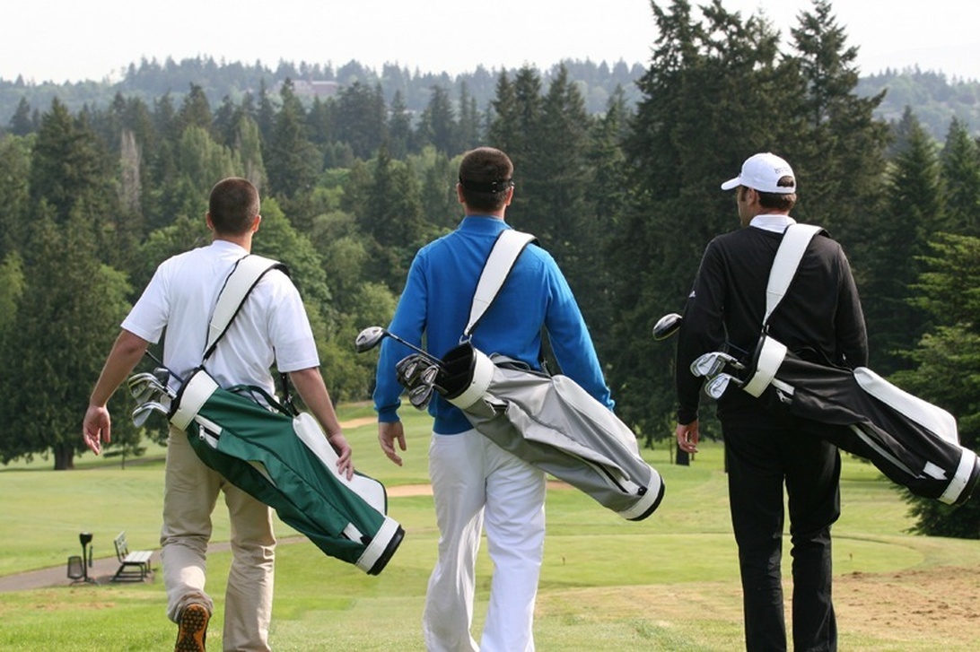 Fyra golfspelare går raskt på fairway mot sina bollar.