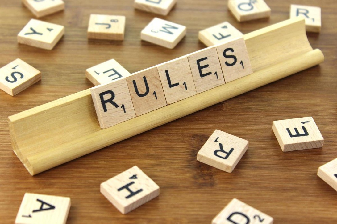 Träbrickor med bokstäver som stavar ordet 'RULES' på en spelbrickshållare, vilket symboliserar vikten av regler.
